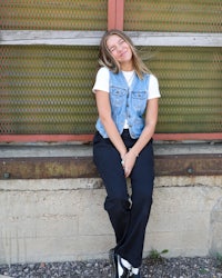 a woman wearing a denim vest sitting on a wall